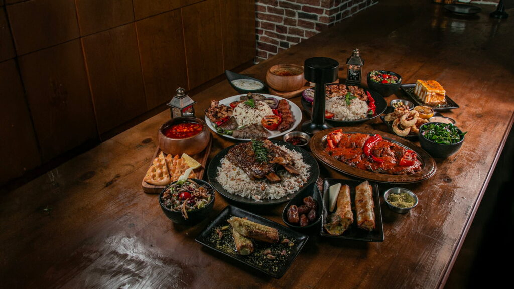 Assorted grilled dishes with rice, salads, and appetizers served on a wooden table.