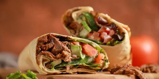 Close-up of a sliced beef shawarma wrap with meat, fresh lettuce, tomato, and cucumber