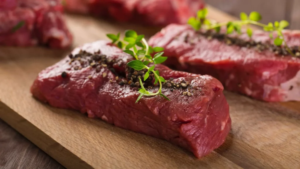 Raw seasoned steak cuts topped with cracked black pepper and fresh thyme on a wooden cutting board