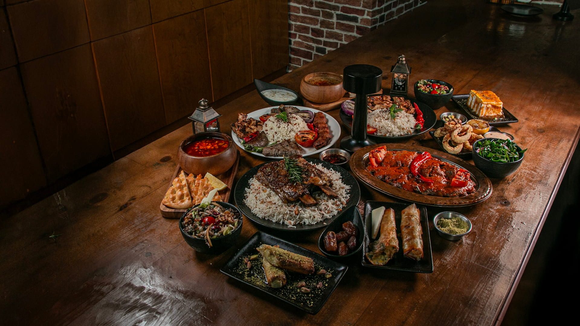 Assorted grilled dishes with rice, salads, and appetizers served on a wooden table.