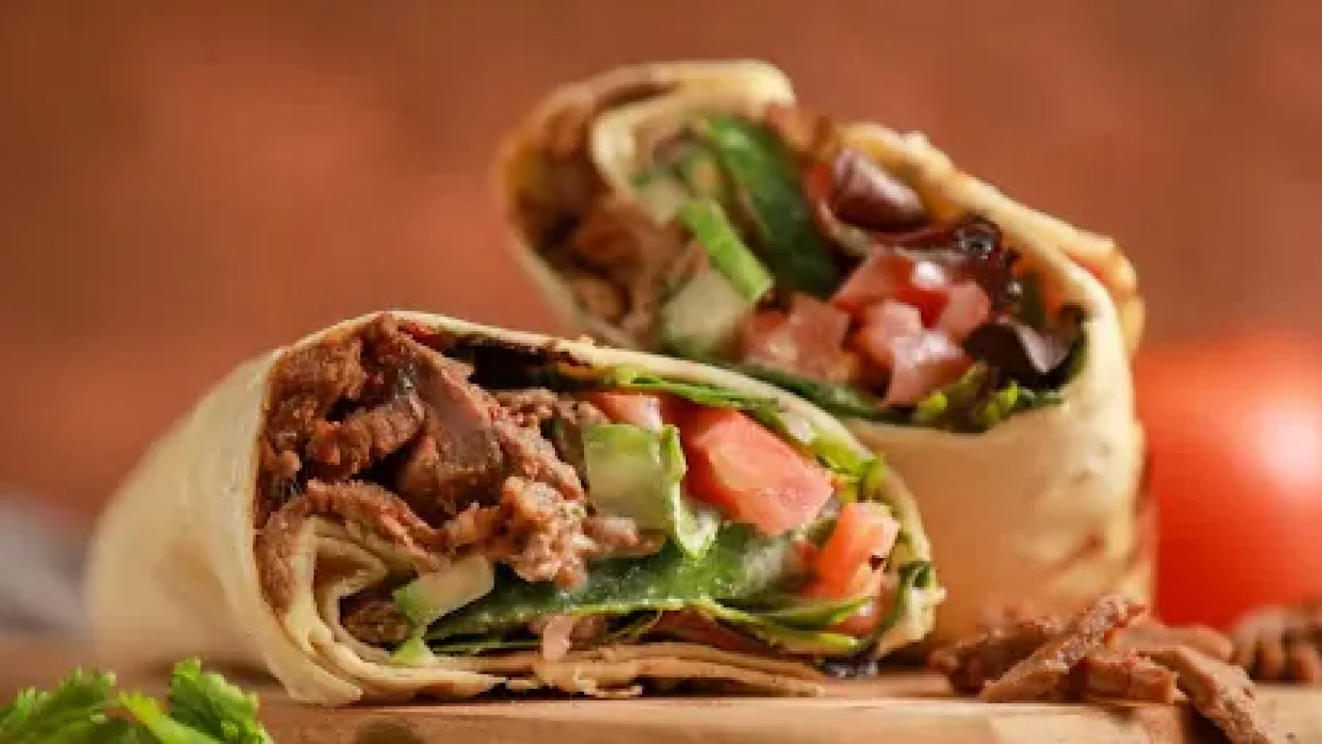 Close-up of a sliced beef shawarma wrap with meat, fresh lettuce, tomato, and cucumber